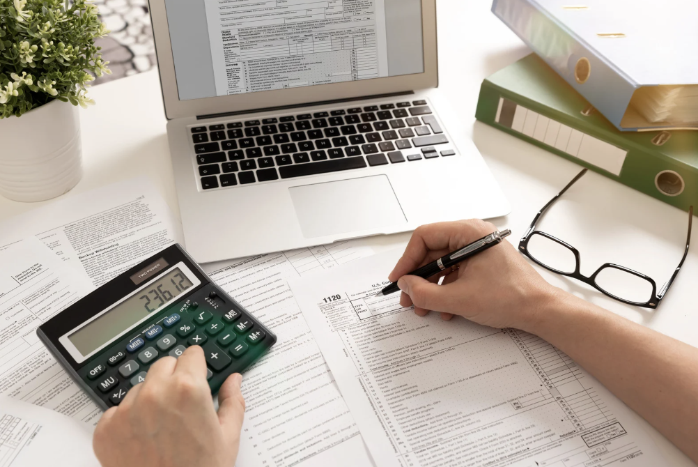 Image of hands with a laptop, a calculator, and a pen.